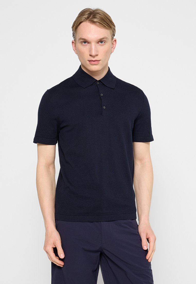 Granatowa dziergana koszulka polo z klasycznym kołnierzykiem, trzema guzikami, krótkimi rękawami i teksturowanym materiałem. Bez widocznych logo i wzorów.