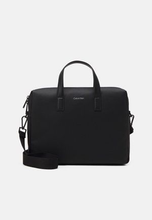Black Calvin Klein briefcase with dual top handles and detachable shoulder strap on white background.