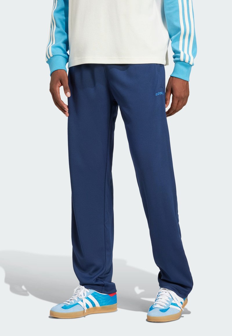Navy blue athletic pants with a smooth texture, elastic waistband, and subtle branding. Paired with light blue sneakers featuring white stripes.