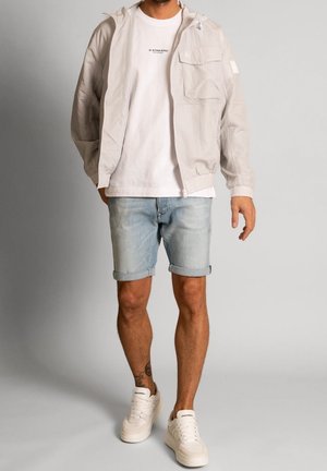 Lysegrå lynlåstrøje med hætte, hvid t-shirt og lyse denimshorts. Har lommer og op-rullede manchetter; kombineret med hvide sneakers.
