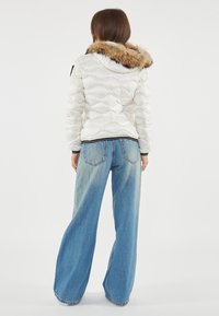 Witte gewatteerde pufferjas met een capuchon met bontafwerking, gecombineerd met lichtblauwe jeans met een wide-leg. Heeft elastische manchetten en een contrasterende tailleband.