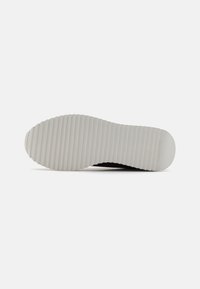 Semelle de sneaker noire avec un motif texturé et strié. Présente un fond en caoutchouc blanc plat pour l'adhérence. Fini lisse, design minimal.