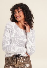 Helles graues, flauschiges Sweatshirt mit weißen Blumenmustern, runder Halslinie und langen Ärmeln, kombiniert mit metallisch goldenen Hosen und einem schwarzen Kordelzug.