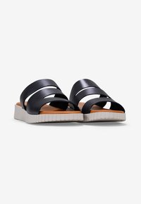 Las sandalias negras de tiras presentan un diseño plano con tres correas superpuestas, una suela blanca texturizada y una plantilla lisa de color marrón claro.