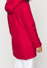 Czerwona ocieplana kurtka z kapturem, długimi rękawami i prostym krojem. Charakteryzuje się przeszyciami i gładką fakturą.