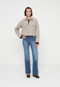 Γκρι κοντό μπουφάν με δύο μπροστινές τσέπες, σε συνδυασμό με μπλε τζιν με καμπάνα. Η εμφάνιση διαθέτει κλείσιμο με φερμουάρ και ολοκληρώνεται με σκούρα παπούτσια.