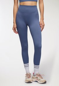 Legginsy w kolorze niebieskim, z wysokim stanem i prążkowaną fakturą, wykonane z elastycznego materiału. W połączeniu z jasnymi sneakersami i białymi skarpetkami w szare paski.