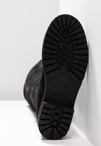 Černá podrážka boty s hlubokými vzory tvaru hvězdy, boční zip a viditelné označení "ANNA FIELD 37" na spodní části.