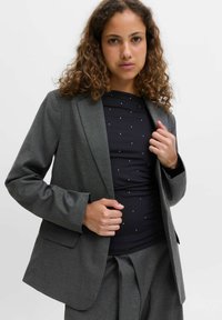 Siva blazer z ozkim črtastim vzorcem, strukturiranimi rameni, zapenjanjem na en gumb in žepljami. Nošen preko temnega zgornjega dela z srebrnimi pikami.