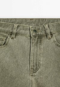 Olivgröna denimjeans med en klassisk femfickdesign, synlig sömnad och en metallknappstängning i midjan.