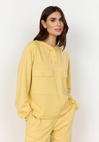 Geel hoodie met twee voorzakken, voorzien van knoopdetails en een ontspannen pasvorm. Zachte textuur en casual ontwerp.