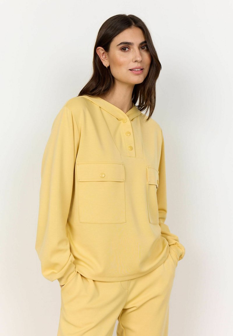 Geel hoodie met twee voorzakken, voorzien van knoopdetails en een ontspannen pasvorm. Zachte textuur en casual ontwerp.
