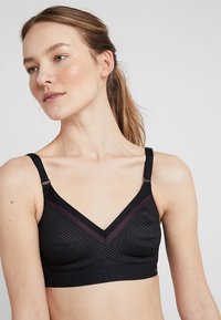 Svart bralette med et teksturert geometrisk mønster, med justerbare stropper, v-hals og vinrøde detaljer langs den øverste kanten.