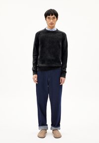 Schwarzer strukturierter Pullover mit geripptem Ausschnitt, kombiniert mit lockeren blauen Jeans, die an den Bündchen gerollt sind, und hellbraunen Schuhen.