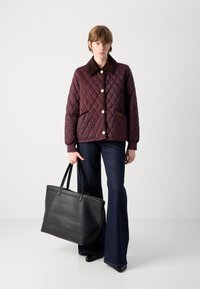 Gepatteerde kastanjebruine jas met een bruine kraag, voorzien van gouden knopen en zakken. Donkere flared jeans en een grote zwarte leren tote bag.