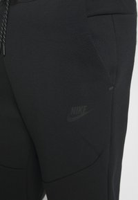Svarta Nike-joggers med en slät textur, elastisk midja, sidofickor och en diskret logotyp på underbenet.