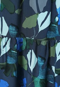 Tissu foncé avec une couture froncée et un motif de feuilles en nuances de vert, bleu, bleu sarcelle et gris.