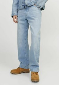 Jean en denim bleu clair avec une coupe droite, associés à des bottes de travail beiges avec des lacets et des semelles en caoutchouc. Design simple, sans motifs.