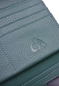 Portafoglio in pelle testurizzata verde con scomparti per carte e logo stampato. Presenta cuciture a contrasto e una finitura liscia.