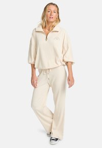 Beige geribbeld loungewear-set met een half-rits pullover met kraag en wijde broek met koord, textuurstof en subtiele branding.