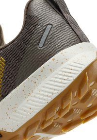 Brown textured sneaker with a white sole featuring splatter accents. The rubber outsole has a patterned grip for traction.