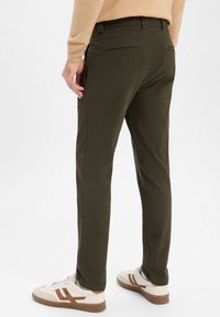 Olijfgroene broek gemaakt van een katoenmix met een gladde textuur, voorzien van achterzakken en een rechte pijp. Gecombineerd met witte sneakers.