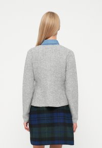 Siv žametni pulover s prilegajočo silhueto, dolgimi rokavi in zaobljenim izrezom, oblečen preko modre karirane krila.