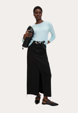 Jasnoniebieski dzianinowy sweter, czarna maxi spódnica dżinsowa z przednim rozcięciem, czarny pasek, czarne płaskie buty z wycięciami, trzyma czarną torbę.