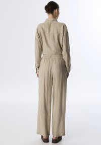 Conjunto de dos piezas color beige hecho de tela texturizada, que incluye una camisa con cuello y pantalones de pierna ancha con cinturilla elástica.