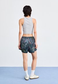Szürke, rövidített tank top, amelyet színes, mintás sportnadrággal viselnek, elasztikus derékkal. A modellen fehér zoknik és sportcipők vannak.