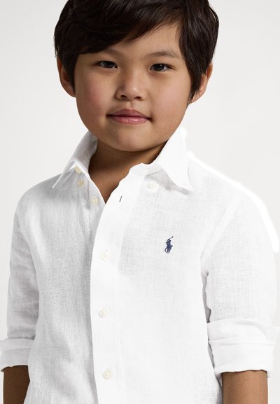 Λευκό πουκάμισο από λινό με γιακά και μανσέτες που έχουν διπλωθεί προς τα πάνω, με μικρό μπλε κεντημένο λογότυπο στο στήθος. Υφασμάτινη υφή, ελαφρύ ύφασμα.