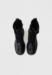 Botas de cuero negro hasta el tobillo con punta redondeada, cordones y un zipper en el costado. Presentan detalles de costura y una textura suave.