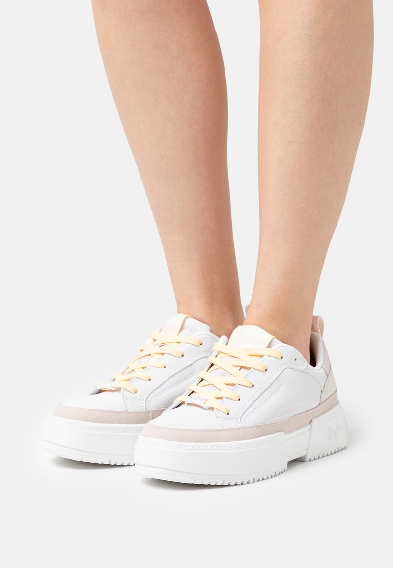 Baskets à plateforme blanches avec des accents rose clair, dotées d'une tige en cuir lisse, de semelles épaisses en caoutchouc et de lacets jaunes.