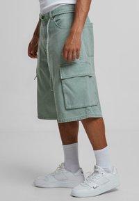 Shorts cargo vert menthe au style décontracté, avec plusieurs poches et une taille à cordon. Assortis à des baskets blanches et des chaussettes.