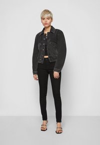 Személy fekete farmerdzsekit, fekete felsőt, fekete skinny nadrágot és fekete, kis tüskés szandált visel.