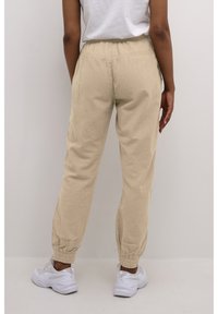 Beige, tapered Hosen aus leichtem Stoff mit elastischem Bund und Bündchen. Getragen mit weißen Sneakers. Minimales Design, keine Muster.