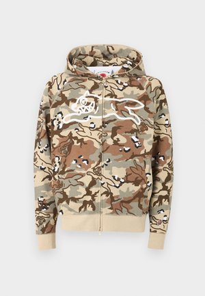 Beige, brun og grønn kamuflasje-hettegenser med glidelås foran, med hvit konturtegning av en løpende tegneseriehund og beige mansjetter og midjebånd.