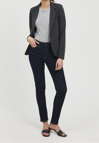 Mörkblå jeans med smal passform, i kombination med en grå t-shirt och en mörkgrå blazer. Outfitten kompletteras av svarta klackar.