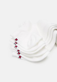 Chaussettes blanches en coton à la cheville empilées, mettant en avant un logo avec des rayures rouges et bleues près de la bordure, affichant une texture lisse et un design simple.