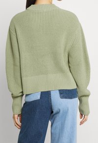 Pull vert clair tricoté avec une coupe ample, des poignets et un ourlet côtelés. Le dos présente un motif texturé et un col rond classique.