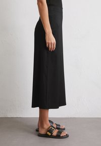 Falda midi negra hecha de una tela suave y ligera, combinada con sandalias negras de tiras con un detalle de hebilla dorada.
