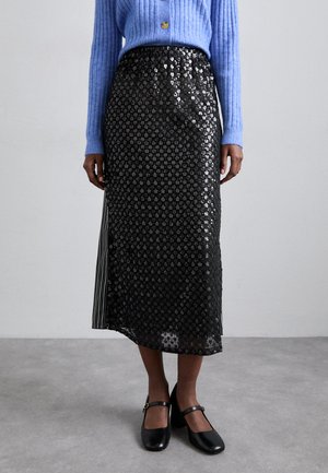 Schwarzer Pailletten-Midirock mit geometrischem Muster, mit vertikalen, gestreiften seitlichen Details, kombiniert mit einem hellblauen gerippten Pullover und schwarzen Schuhen.