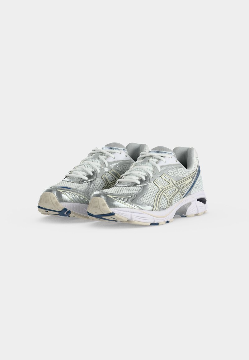 Par de zapatillas deportivas plateadas y blancas con cordones blancos y detalles azules, exhibidas sobre un fondo blanco.