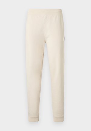 Pantaloni sport crem, cu croială slim, talie elastică și manșete, având un mic logo negru pe coapsa superioară.