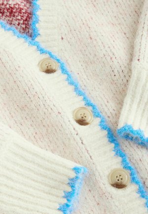 Nööbitav kreemjas villane kardigan roosakate täppidega. Omab helesinist lainelist äärist ja ümarad beežid nööbid soonelisel pinnal.
