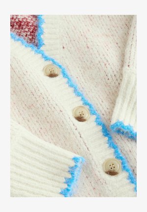 Krekla stila kardigans krēmkrāsas vilnā ar rozā punktiem. Izceļas ar gaisīgi zilu viļņotu apmali un apaļām bēšām pogām uz ribotas tekstūras.