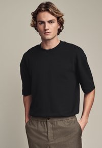 Zwarte t-shirt met korte mouwen, gemaakt van zachte stof, met een ronde hals en een losse pasvorm, gecombineerd met lichtbruine textuurbroek.