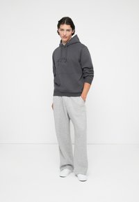 Sudadera con capucha gris, con un bolsillo frontal y texto en relieve, combinada con pantalones de chándal gris claro con rayas laterales. Ambos hechos de una tela suave.