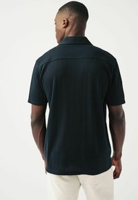 Camicetta nera a maniche corte con un design testurizzato a coste, caratterizzata da un colletto classico e un orlo dritto. Stile semplice e funzionale.