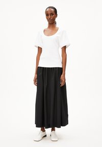 Weißes geripptes Oberteil mit kurzen Puffärmeln, kombiniert mit einem schwarzen plissierten Rock und weißen Schnürschuhen. Einfaches, klares Design.